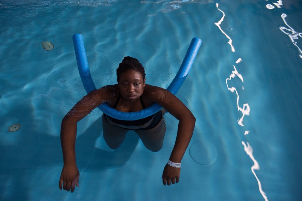 Eine schwarze Frau ist in einem Schwimmbad und liegt auf einer blauen Poolnudel.