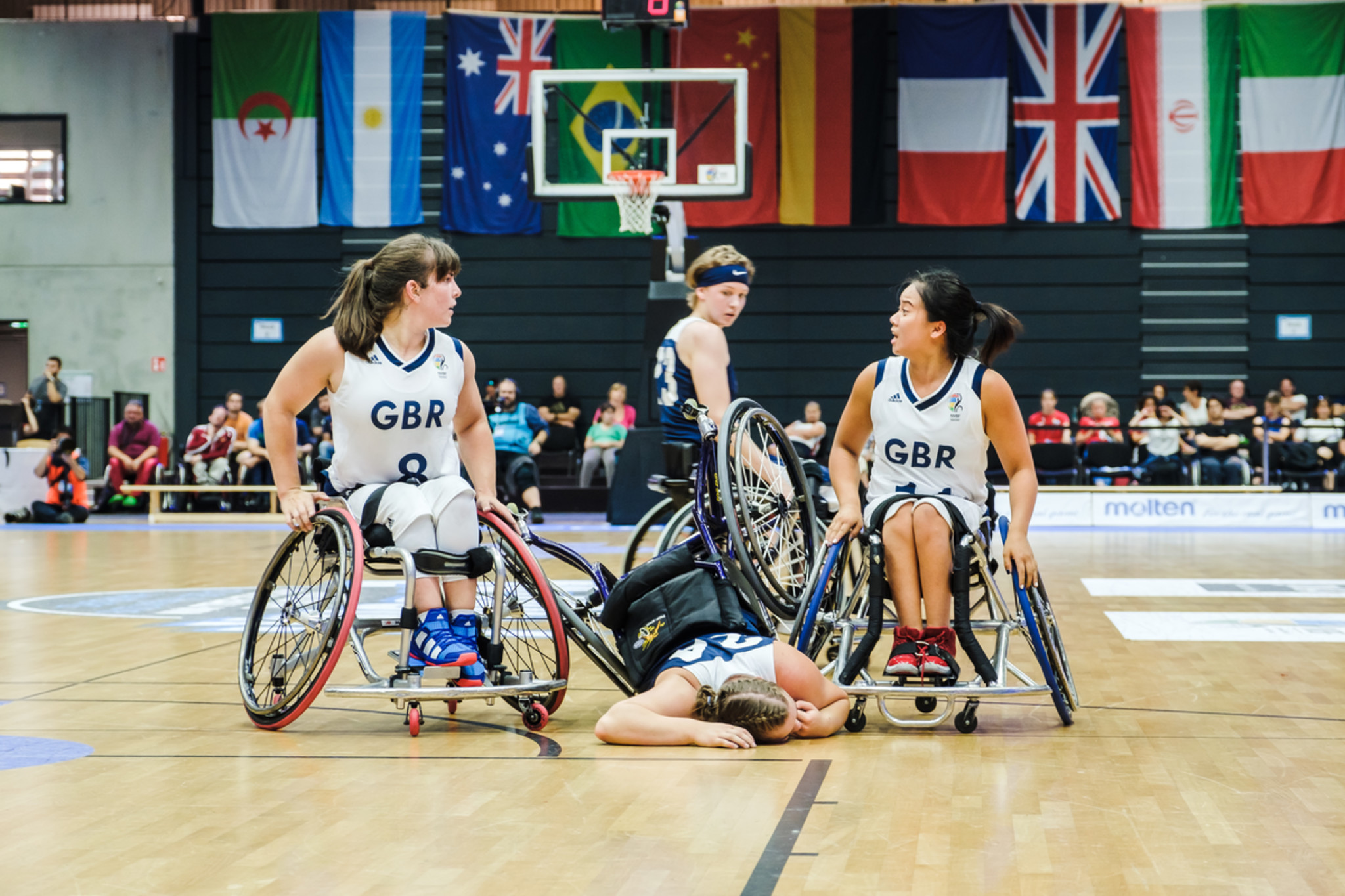 Frauen spielen Rollstuhlbasketball. Eine liegt am Boden im Rollstuhl und verzieht schmerzhaft das Gesicht.