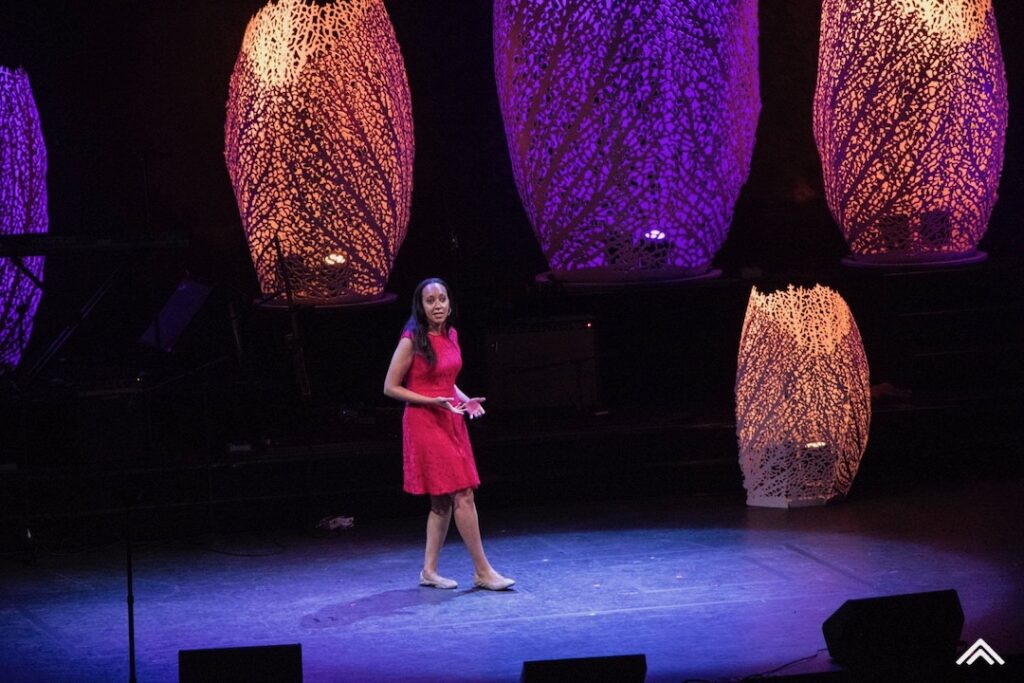 Haben steht in einem roten Kleid auf einer großen Bühne und hält eine Rede.