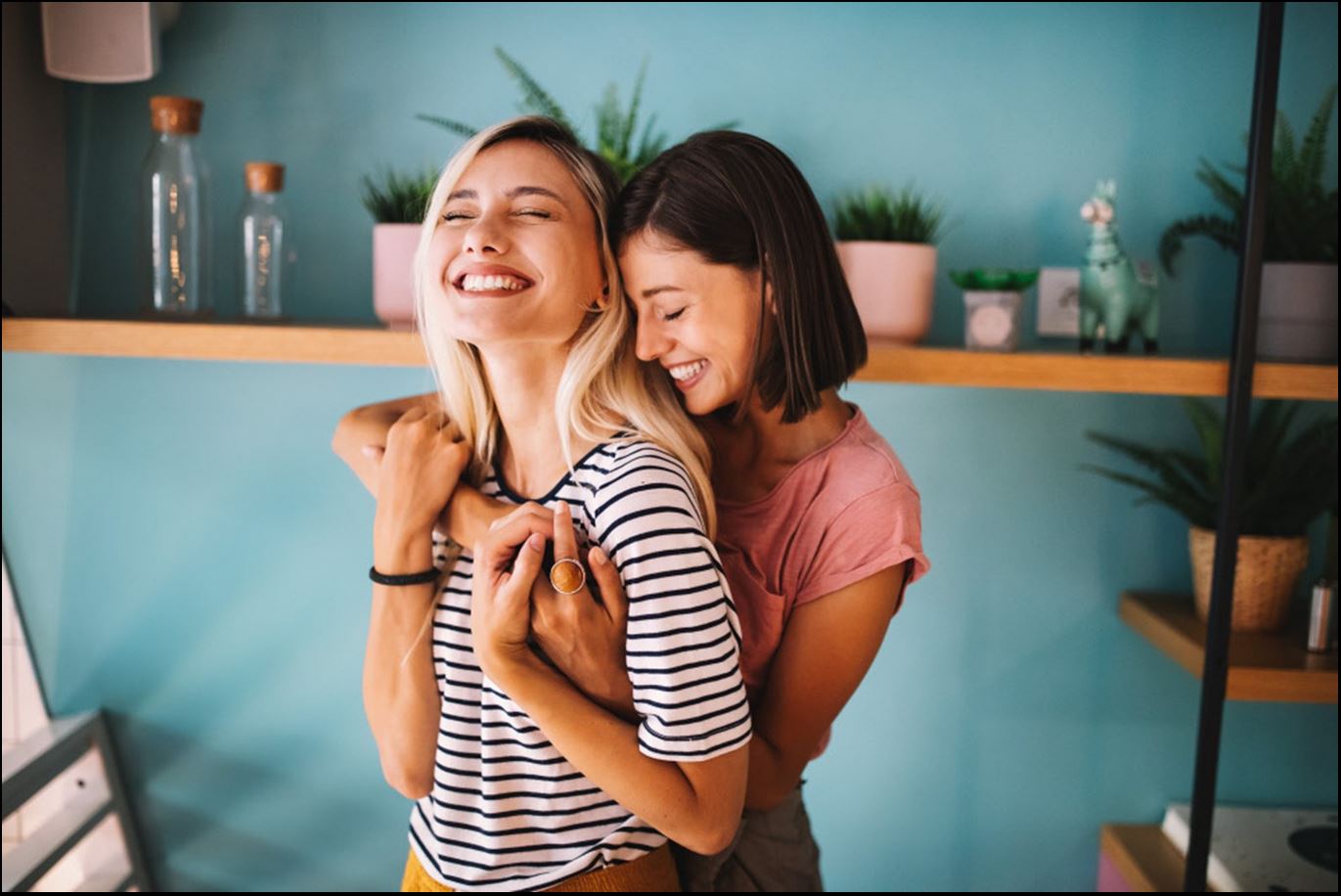 Zwei Frauen umarmen sich breit grinsend und halten dabei Händchen.
