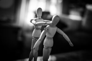 Schwarz-weiß Foto von zwei Holzfiguren. Die eine Figur würgt die andere.