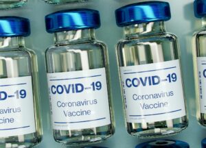 Mehrere kleine medizinische Glasflaschen mit blauem Deckel un der Aufschrift "Covid-19" liegen auf einem Tablett.