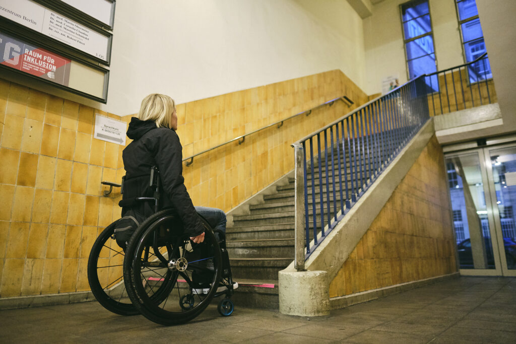 Eine Frau sitzt im Rollstuhl vor einer großen Treppe.