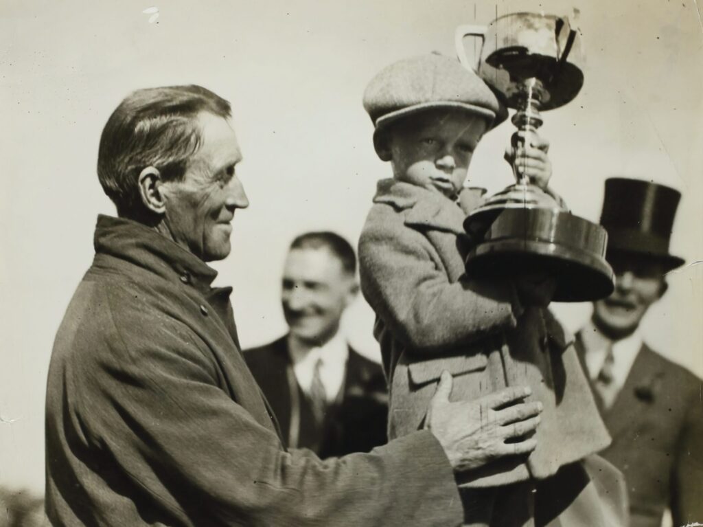 Ein altes Bild von einem alten Mann, der einen kleinen Jungen mit Pokal hochhält.
