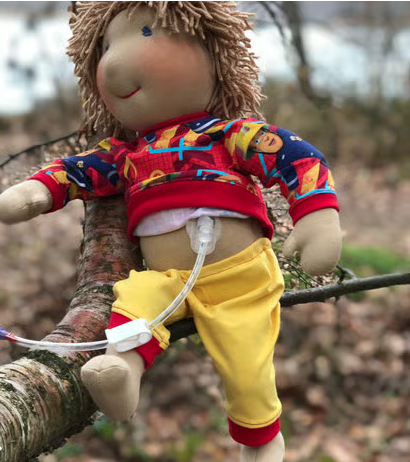 Puppe mit gelber Hose und Paw Patrol Oberteil sitzt auf kleinem Zweig im Baum, im Hintergrund Wald.