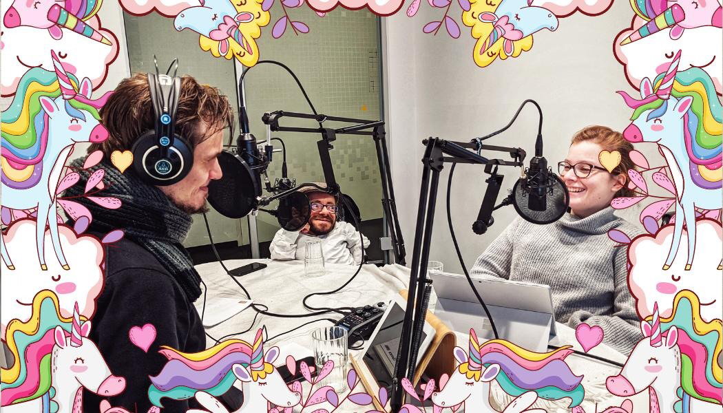 Judyta, Jonas und Raul sitzen an einem Tisch und nehmen den Podcast auf. Um das Bild herum ist ein rosa Rand mit Einhörnern und regenbogen.