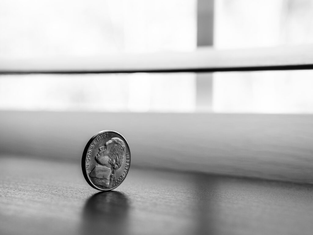Ein schwarz-weißes Foto. Eine Münze rollt auf einem Tisch.