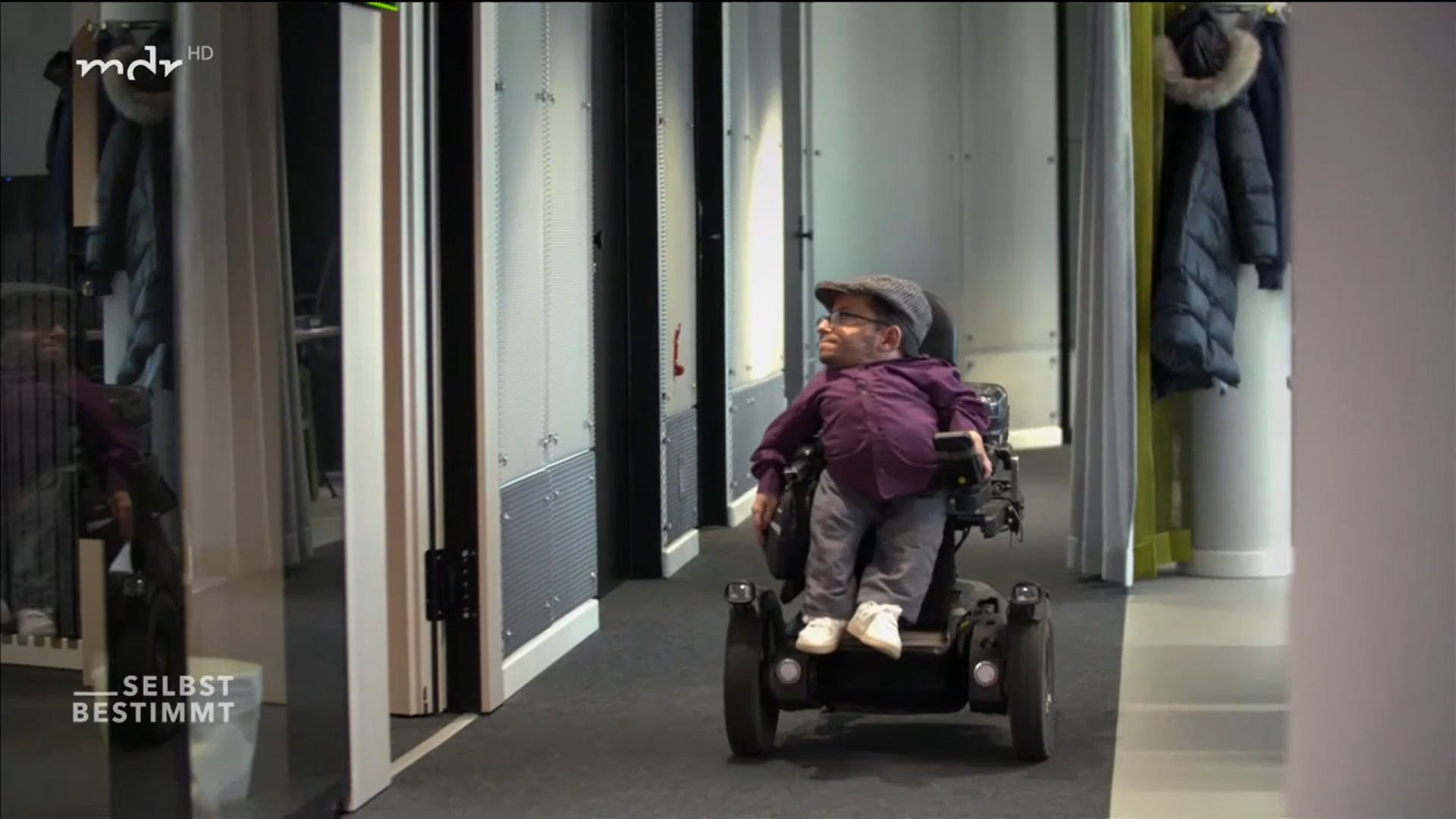 Foto von Raul, der in seinem Rollstuhl einen Bürogang entlangfährt.