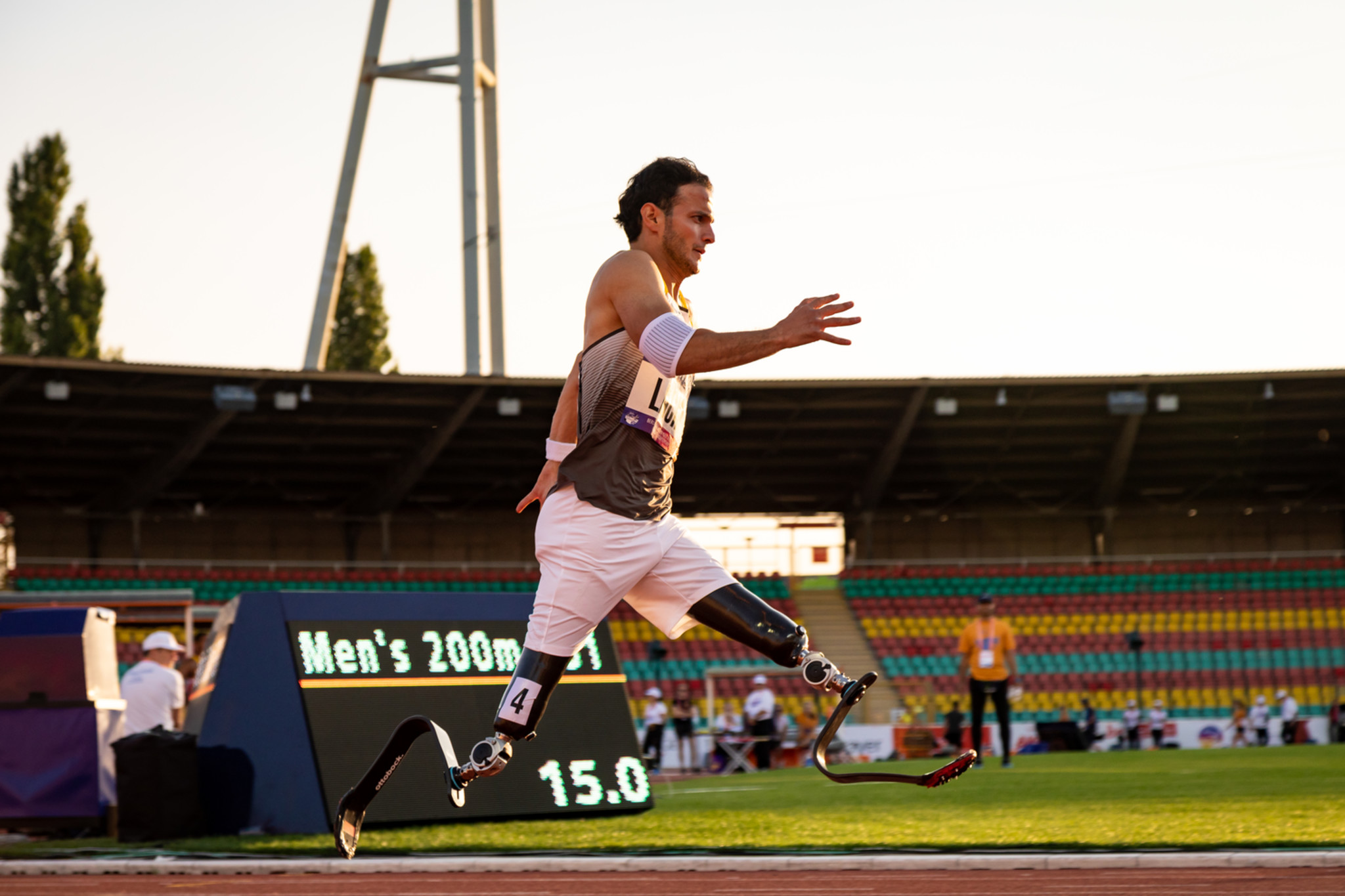 Ein Leichtathlet rennt im Sonnenschein durch ein Stadion. Er trägt zwei Beinprothesen.