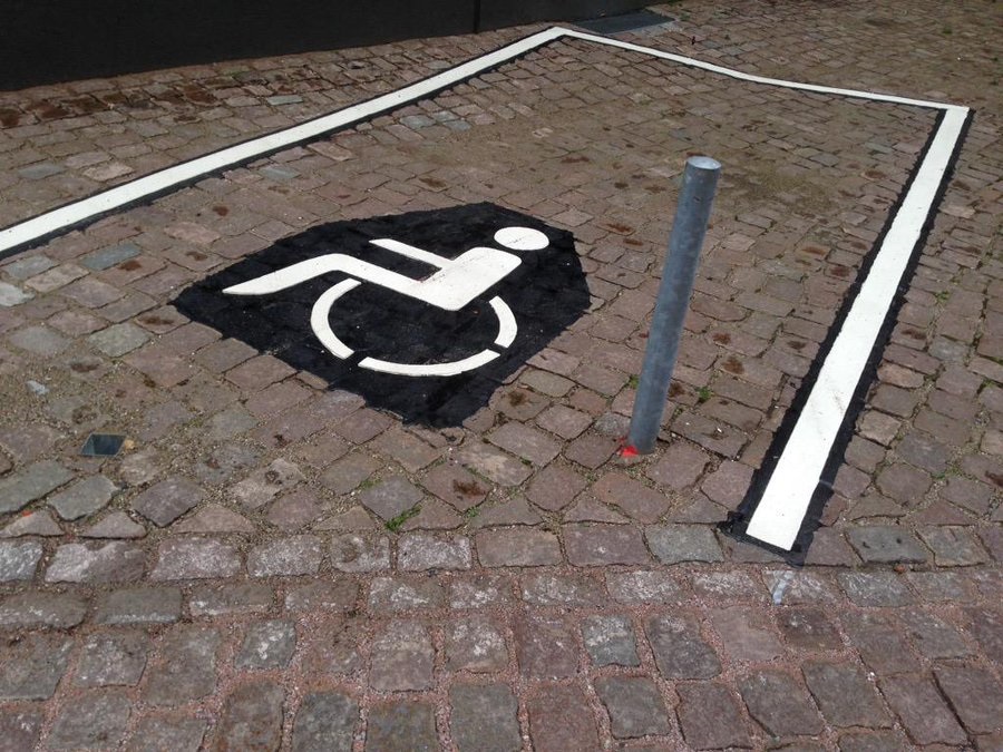 Auf einem Behindertenparkplatz ist ein Poller einbetoniert.