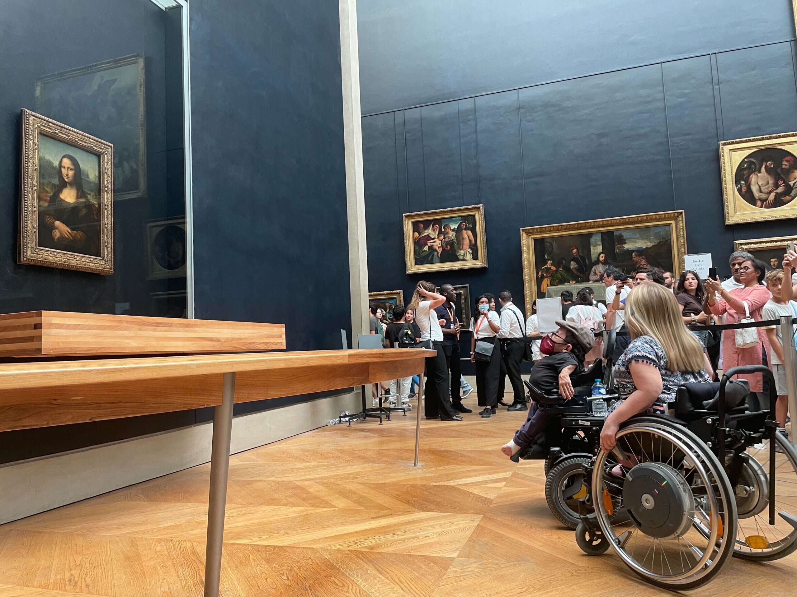 Raul im Rollstuhl vor der Mona Lisa im Louvre in Paris. Er ist vor der Absperrung, die die anderen Bucher*innen vom Gemälde trennt.