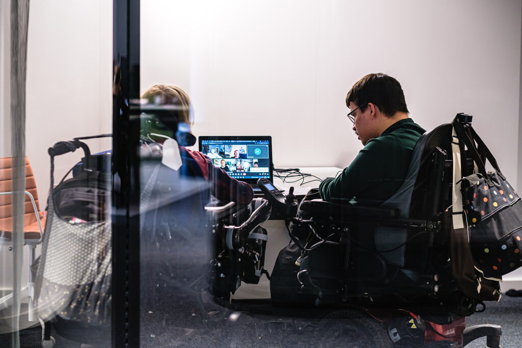 Zwei Personen im Rollstuhl sitzen in einem Büro vor einem Laptop.