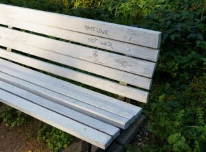 Auf einer Holzbank steht geschrieben: Make love not war. Daneben das gemalte Peace-Zeichen.