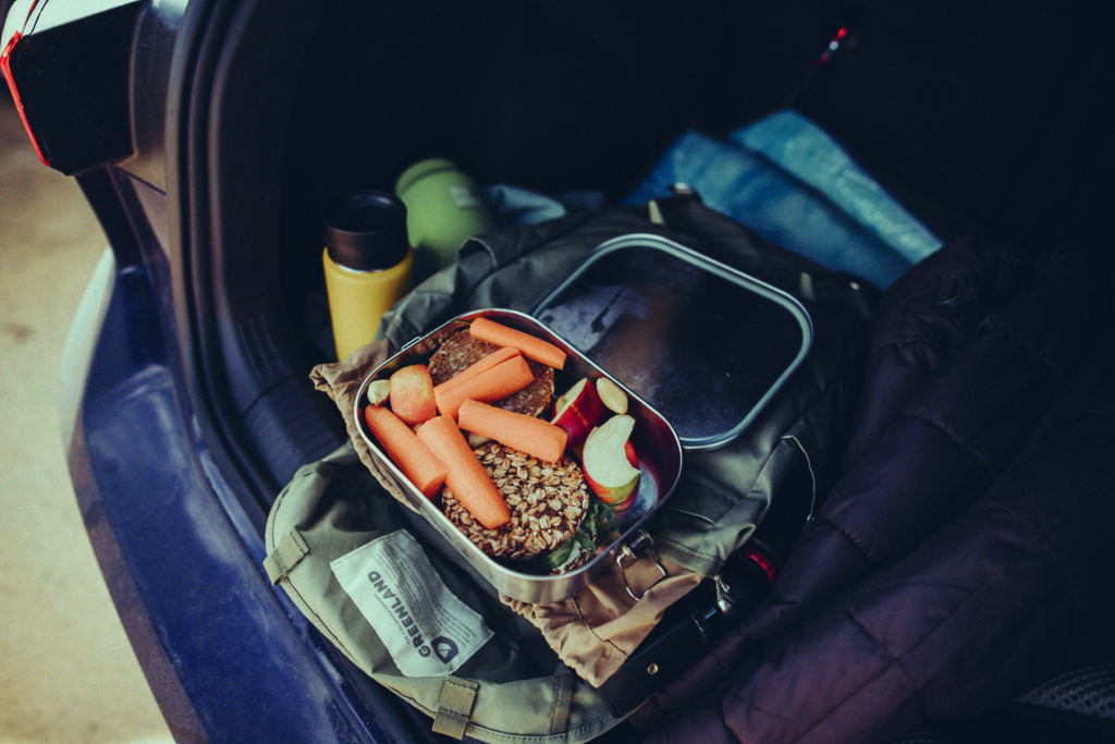 In einem Rucksack liegt eine geöffnete Brotdose mit geschnittenen Äpfeln und Möhren.