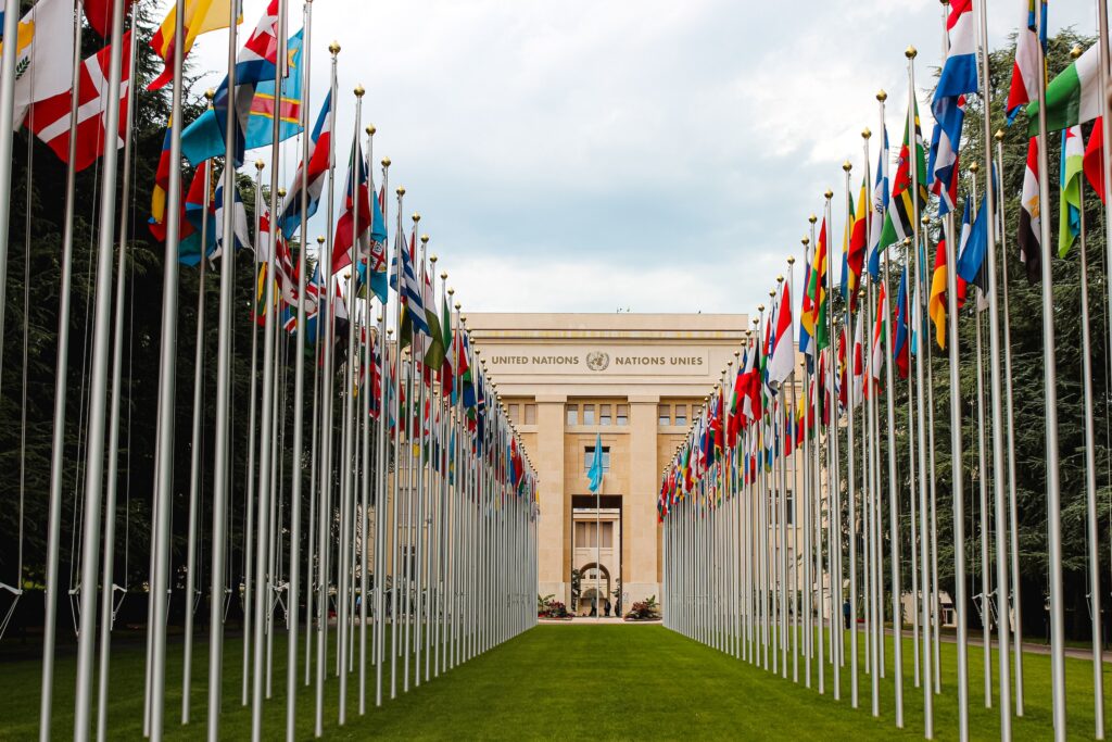 Blick auf das Gebäude der Vereinten Nationen. Links und rechts eine Allee aus Fahnen der Mitgliedsstaaten.