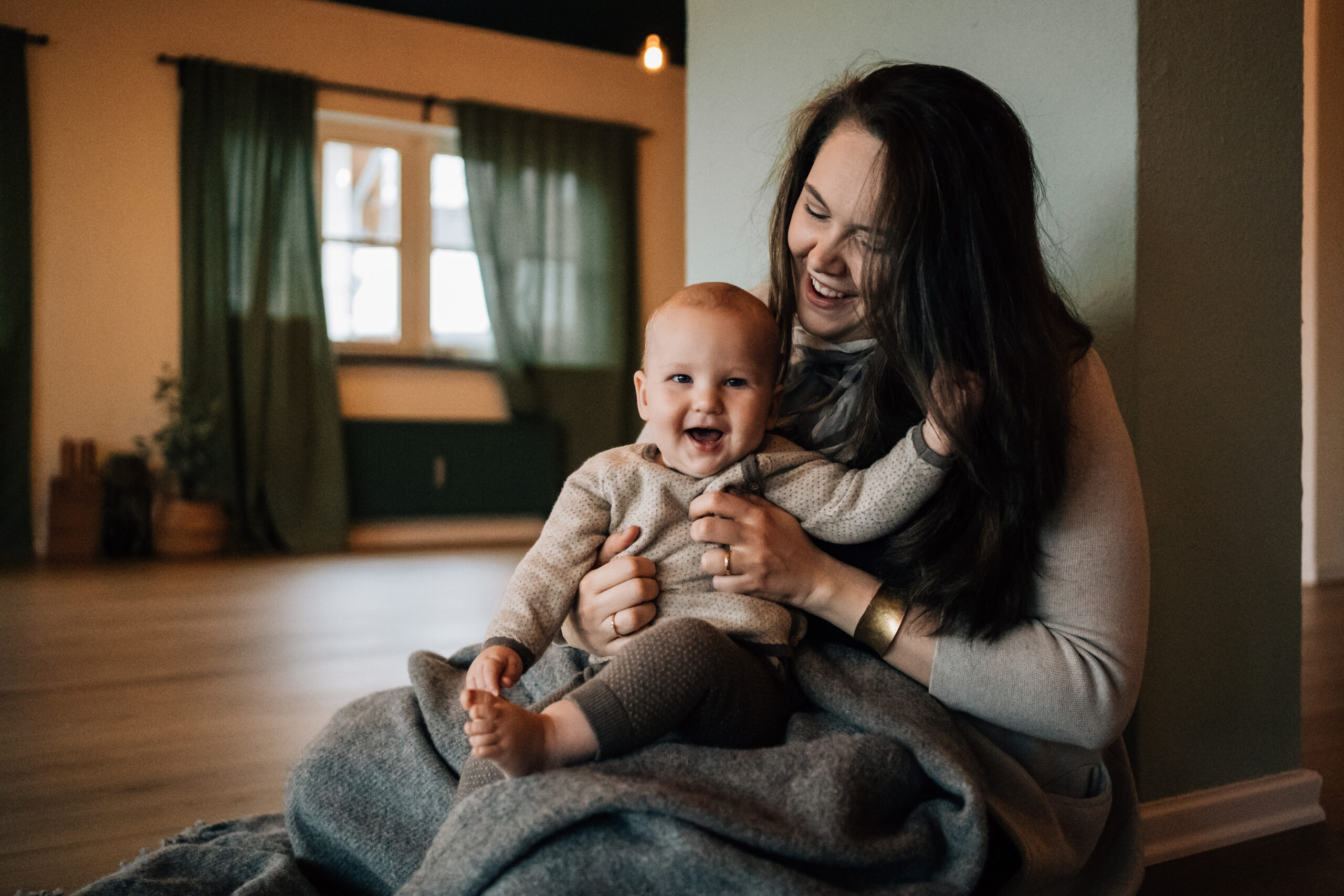 Eine Frau mit dunklen langen Haaren hält ein Baby vor sich. Das Baby lacht herzlich.