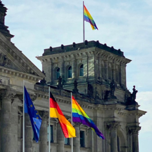 Ein Teil des Bundestages ist zu sehen mit drei Flaggen: Europa, Deutschland und die Pride-Flagge.