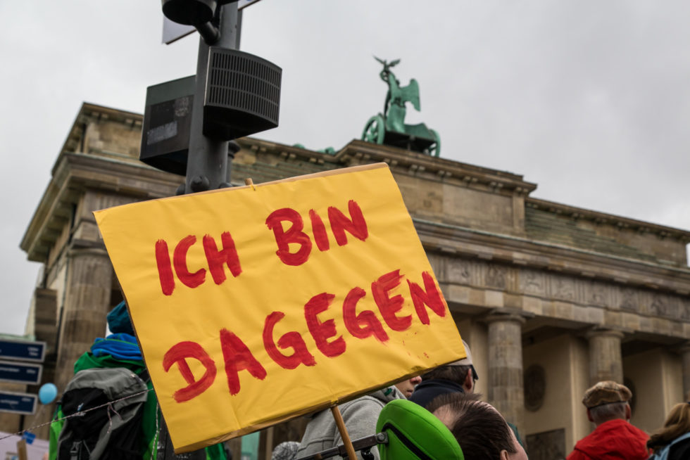 Vor dem Brandenburger Tor wird en Schild hochgehalten auf dem "ich bin dagegen" steht.
