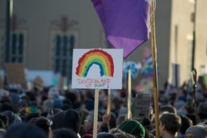 Die Köpfe und Mützen einer großen Menschenmenge ist zu sehen, mittig sehr präsent ein Transparent, auf dem ein Regenbogen gemalt ist mit den Worten „Deutschland ist bunt“.