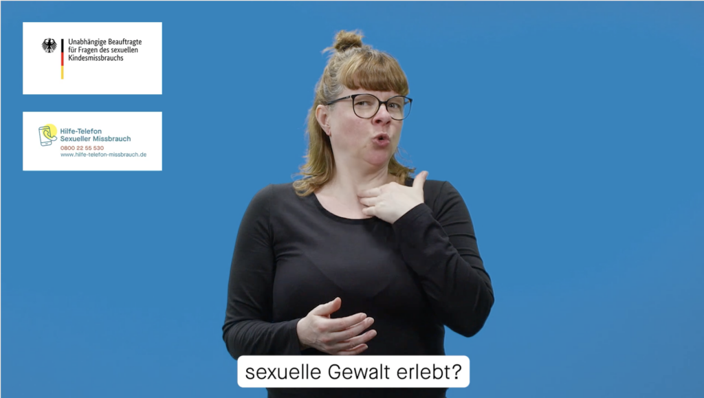 Eine Frau im schwarzen Pullover gebärdet vor einem blauen Hintergrund.