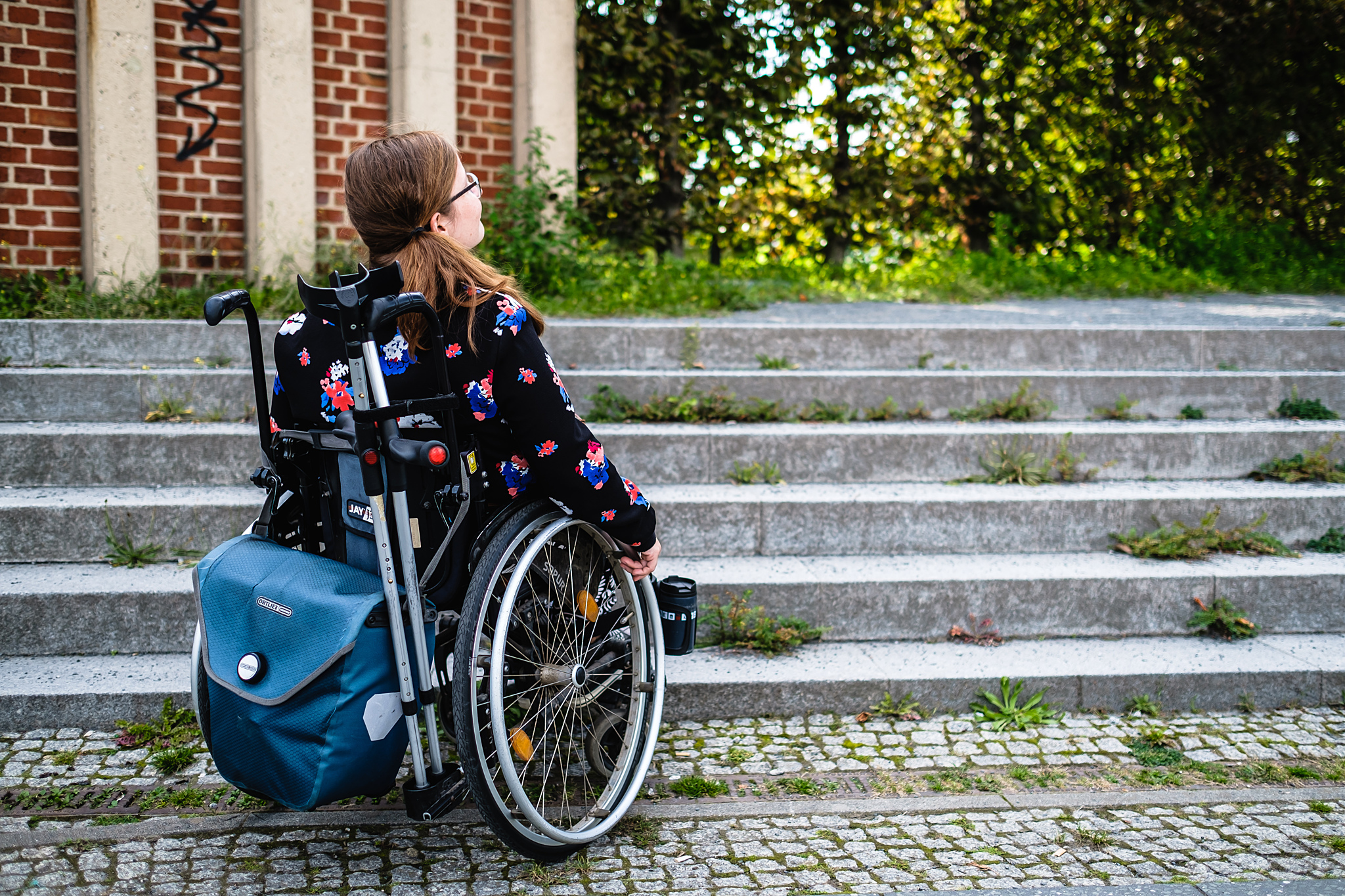 Eine Frau im Rollstuhl vor einer 6-stufigen Steintreppe.