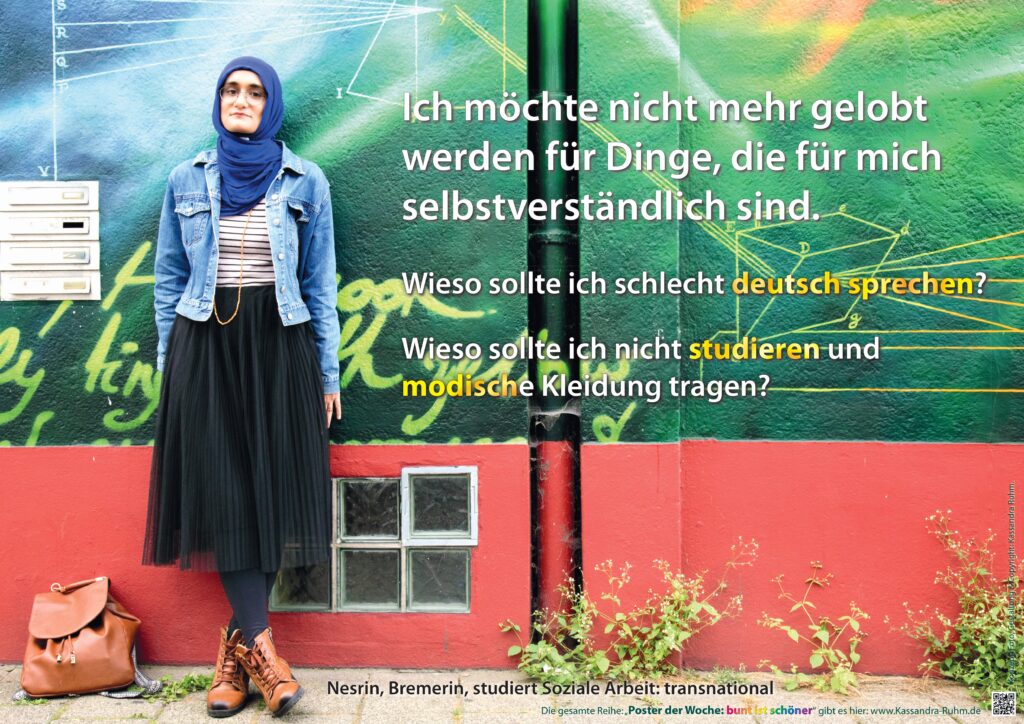 Ein Frau in Jeansjacke, blau-weiß gestreiftem Shirt, schwarzem Faltenrock, schwarzer Leggings, braunen Stiefeln, Brille und Kopftuch lehnt an eine bunte Hauswand. Darüber der Text: „Ich möchte nicht mehr gelobt werden für Dinge, die für mich selbstverständlich sind. Wieso sollte ich schlecht Deutsch sprechen? Wieso sollte ich nicht studieren und modische Kleidung tragen? Nasrin, Bremerin, studiert Soziale Arbeit.