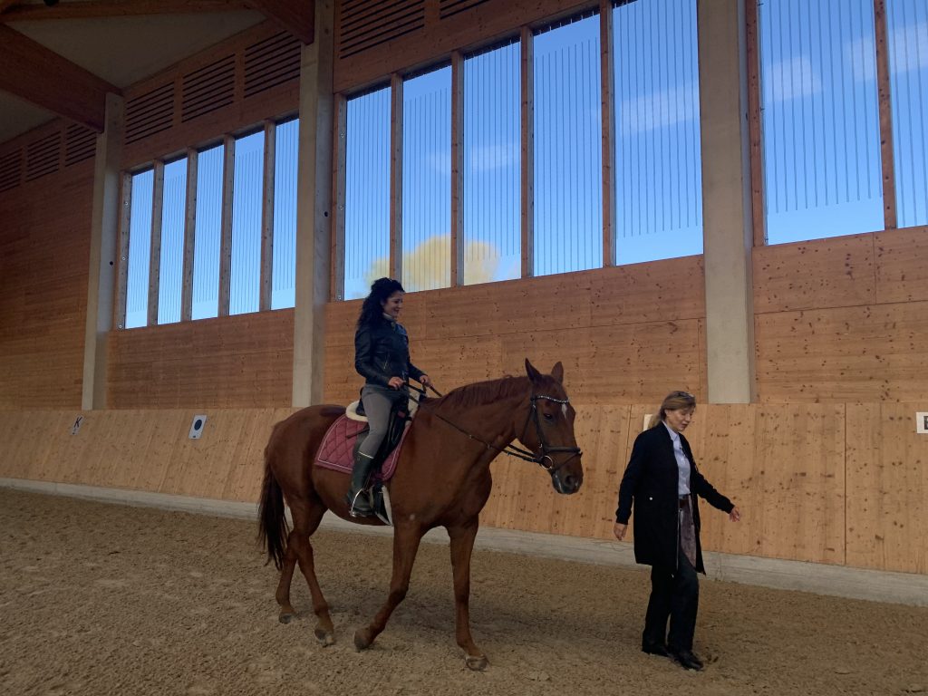 Senatorin Kiziltepe sitzt auf einem Pferd und reitet in einer Halle, Friederike Wendt läuft nebenher.