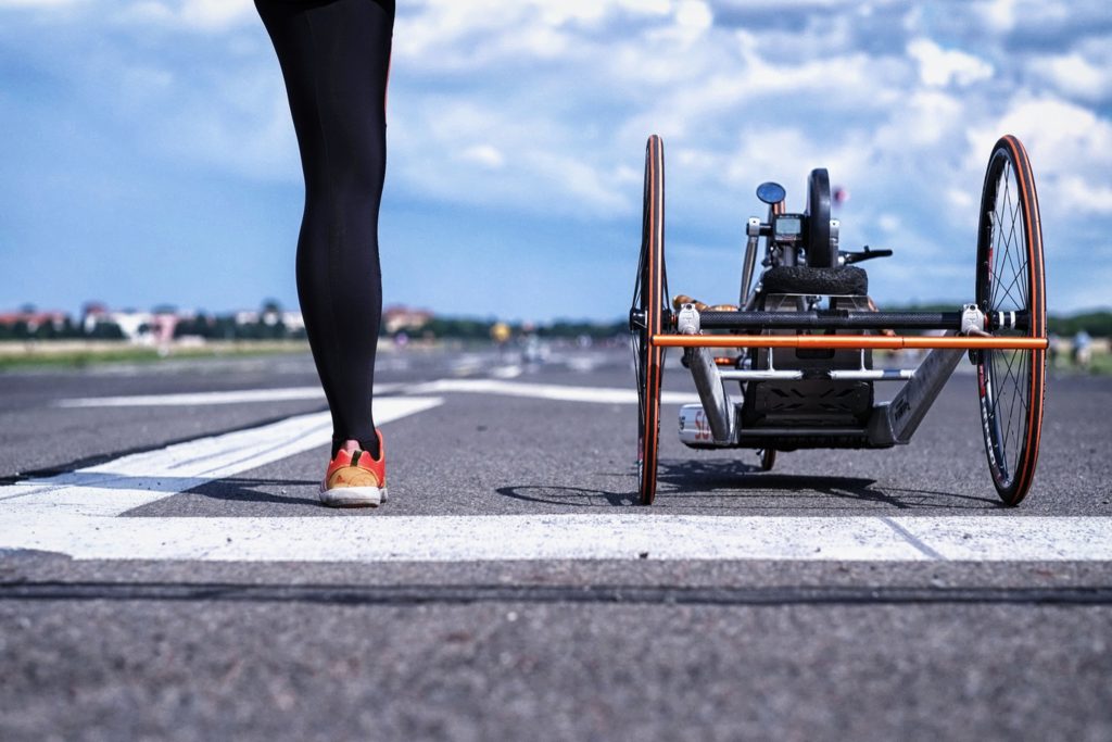 Eine Person mit einem Bein steht auf einem Rollfeld, neben ihr ein professionelles Handbike.