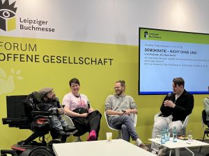 Raúl Krauthausen, Karina Sturm, Arne Semsrott und Jonas Karpa sitzen auf einer Bühne der Leipziger Buchmesse und halten Mikrofone in der Hand.