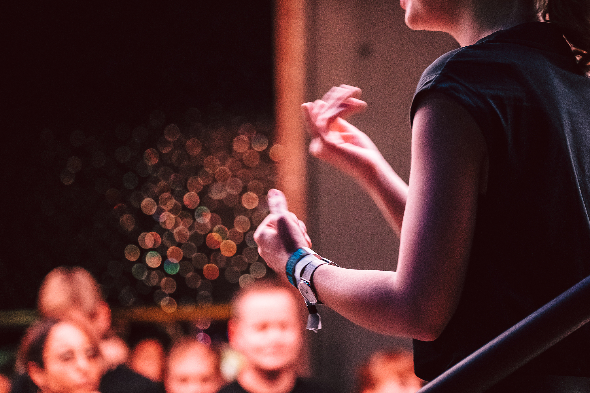 Abendliche Bühnenstimmung, im Vordergrund gebärdet eine Person auf einer Bühne, Hände und ein Teil des Oberkörpers sind zu sehen, im Hintergrund sitzendes Publikum.