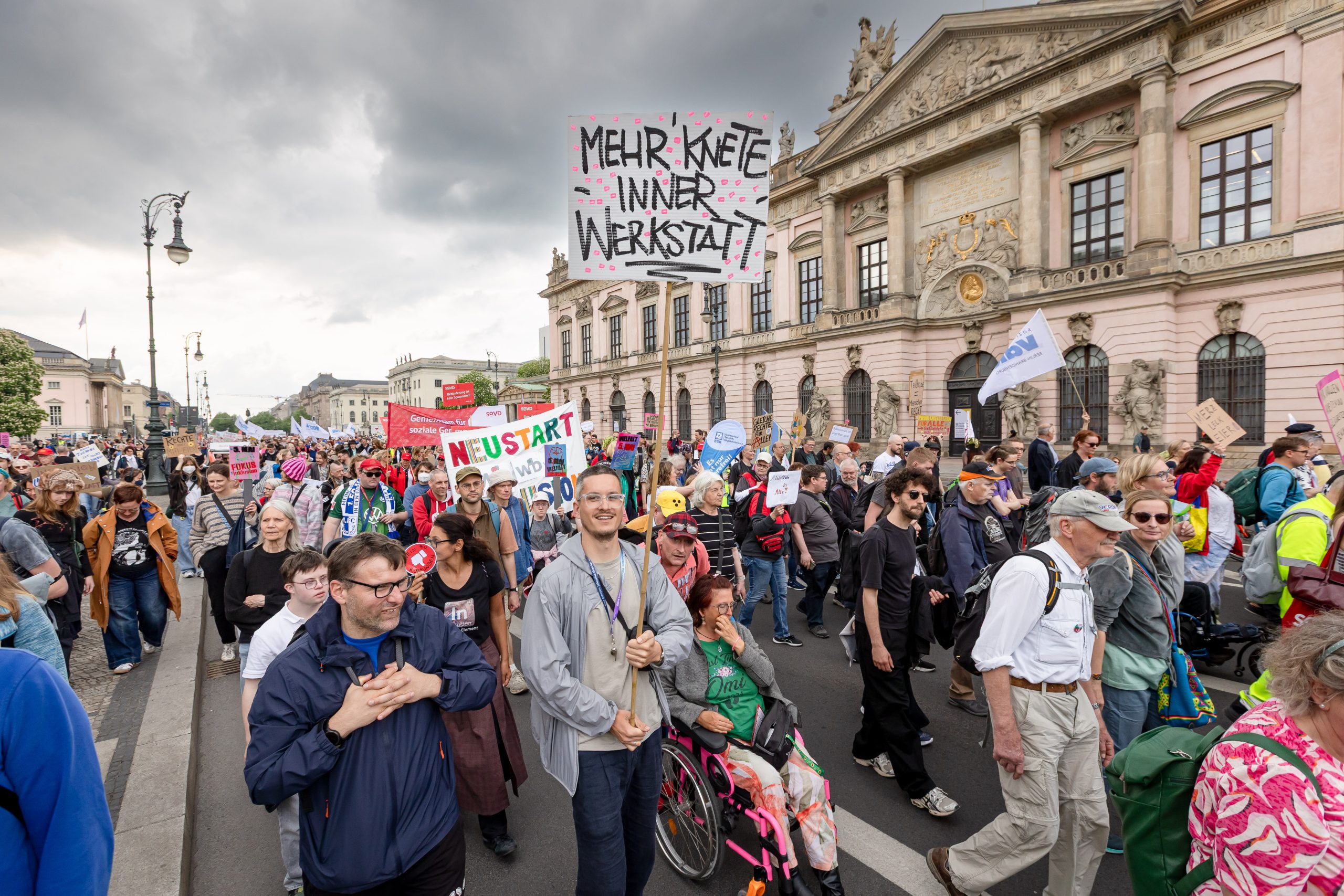 Demo am 5. Mai in Berlin zum Europäischen Protesstag für die Gleichstellung von Menschen mit Behinderungen. Eine Person trägt ein Plakat mit der Aufschrift: Mehr Knete inner Werkstatt.