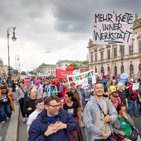 Demo am 5. Mai in Berlin zum Europäischen Protesstag für die Gleichstellung von Menschen mit Behinderungen. Eine Person trägt ein Plakat mit der Aufschrift: Mehr Knete inner Werkstatt.