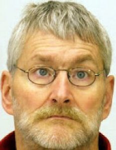 Porträt einer weiß gelesenen Person mit Brille, kurzen, grauen Haaren und Bart.