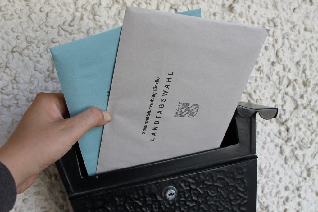 Eine Hand wirft Briefwahlunterlagen in einen Briefkasten.