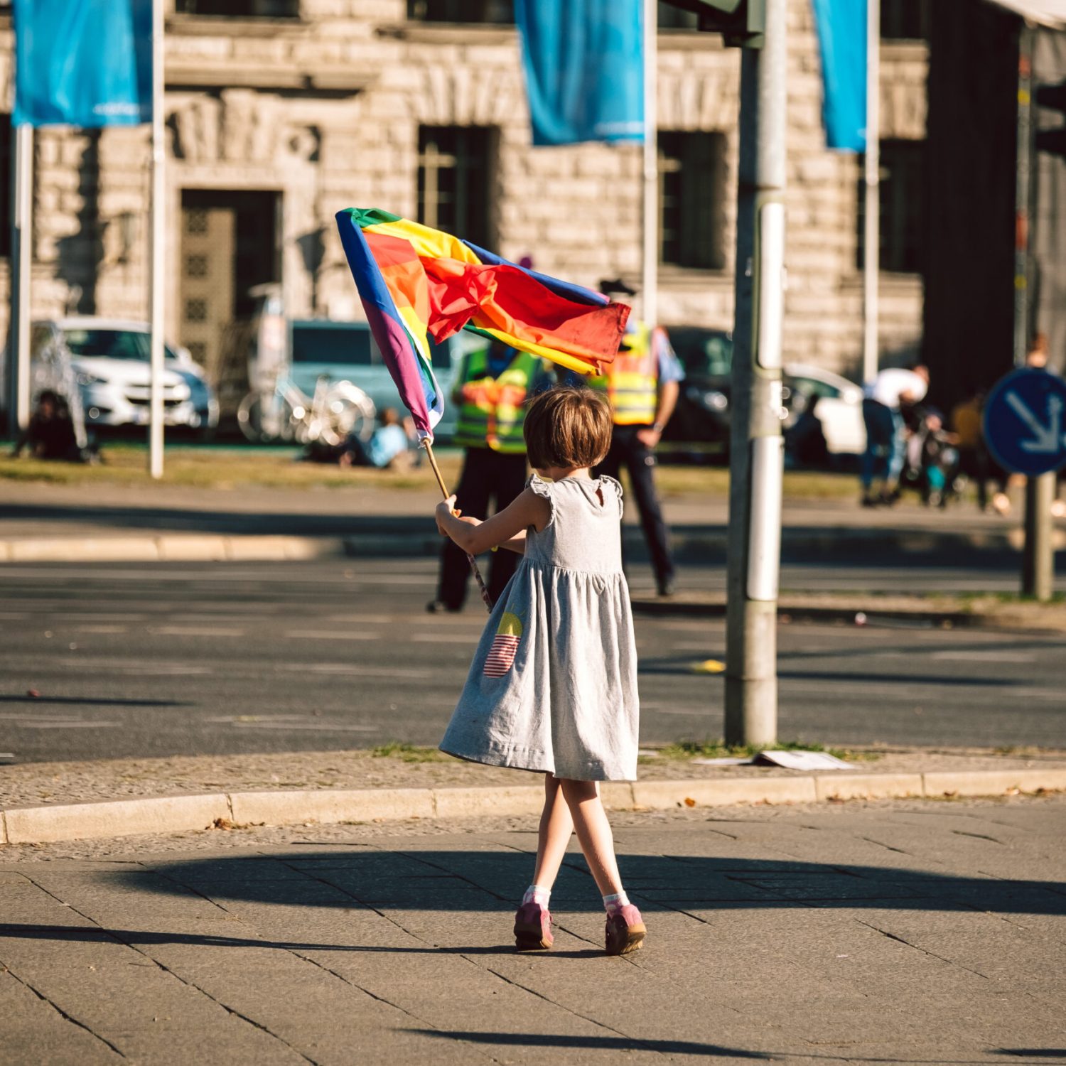 #Unteilbar Demo 2018 in Berlin Ein junges Mädchen in einem weißen Sommerkleid ist von hinten zu sehen. Sie szeht auf der Straße und schwenkt eine bunte Fahne.
